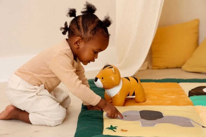 Niño jugando con un tigre de peluche de Little Big Friends sobre una alfombra colorida.